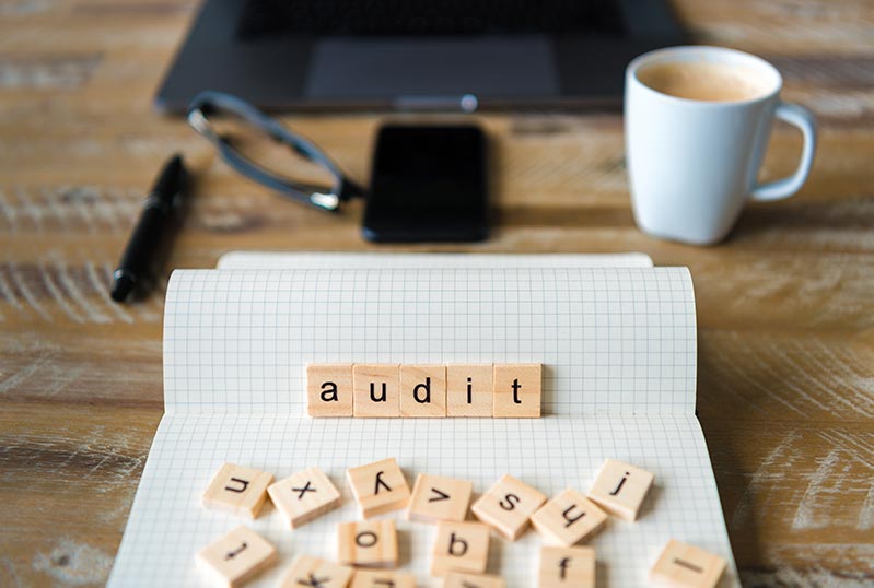 ATO Audit and Disputes - Closeup on notebook over wood table background, focus on wooden blocks with letters making Audit word